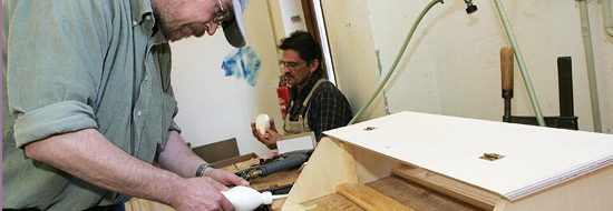 Darstellung von zwei Personen, eine Person arbeitet mit Holz